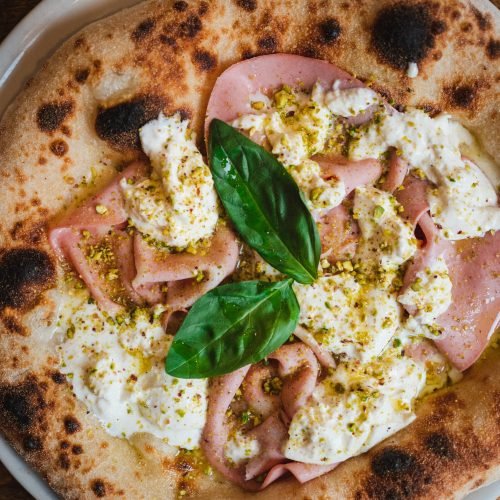 Top view of an authentic italian pizza. It has mozzarella, burrata , mortadella and pistachios.